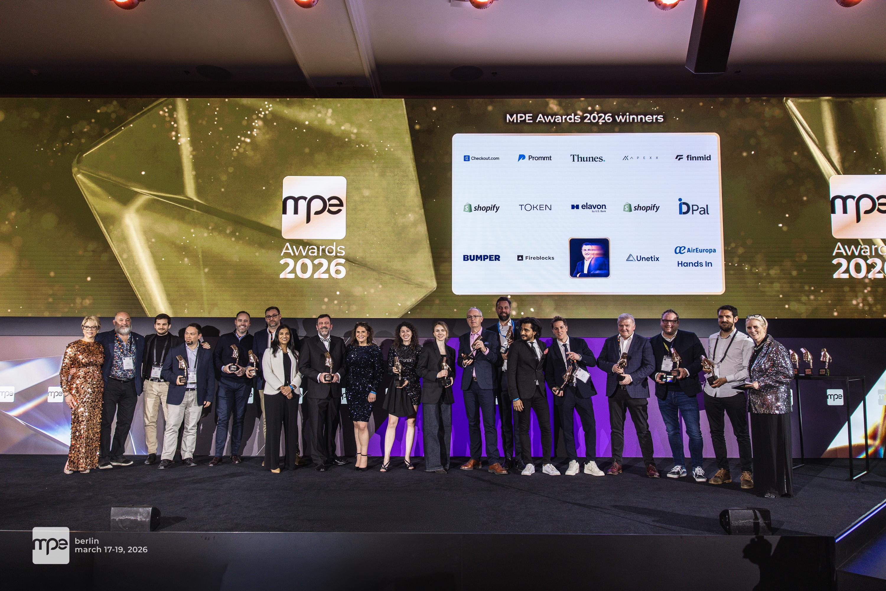 Group of people holding trophies on stage at the MPE Awards 2026 in Berlin, with a large screen displaying winners' logos.
